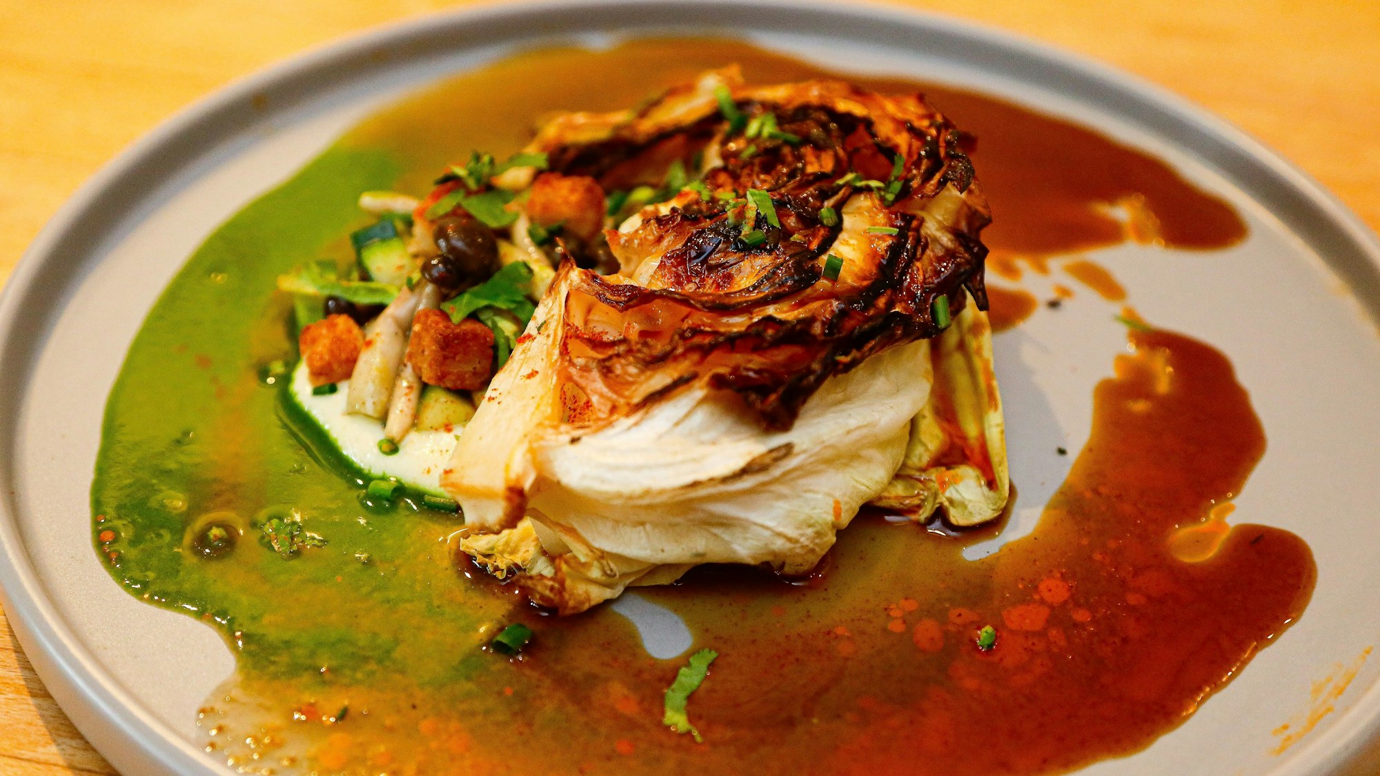 Gegrillter Spitzkohl mit Shimeji-Pilzen, Chili-Jus und Croûtons auf einem Teller.