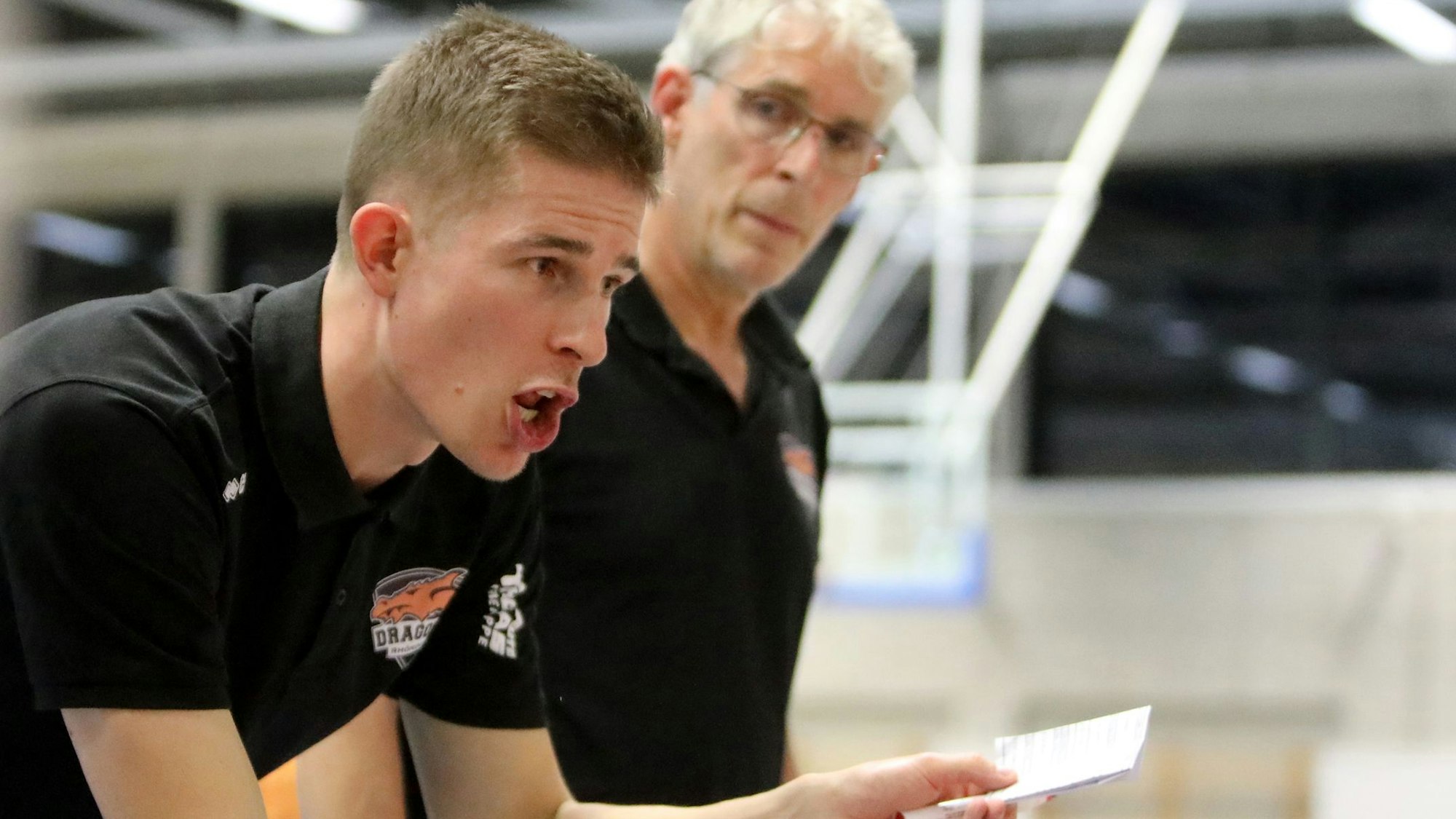 Der Rhöndorfer Cheftrainer Julius Thomas (vorne) hält einen Zettel in der Hand und instruiert seine Spieler. Co-Trainer Martin Otto hört aufmerksam zu.