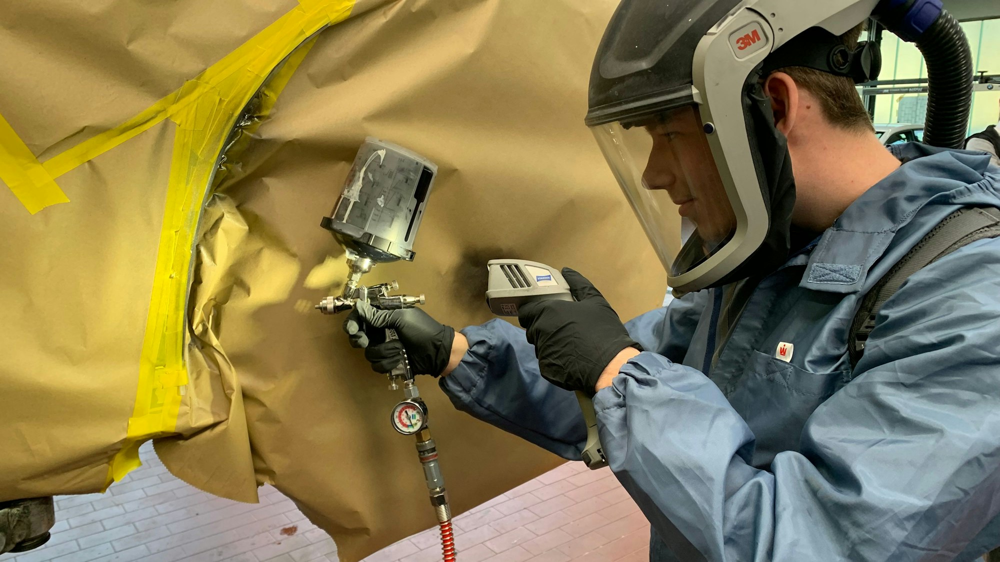 Yannic Lülsdorf arbeitet mit einer Farbspritzpistole an einem Fahrzeugteil.