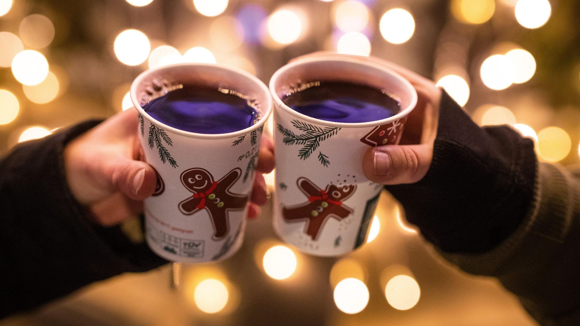 Zwei Frauen stoßen am Schlossplatz mit Glühwein gefüllten Bechern an. Symbolbild