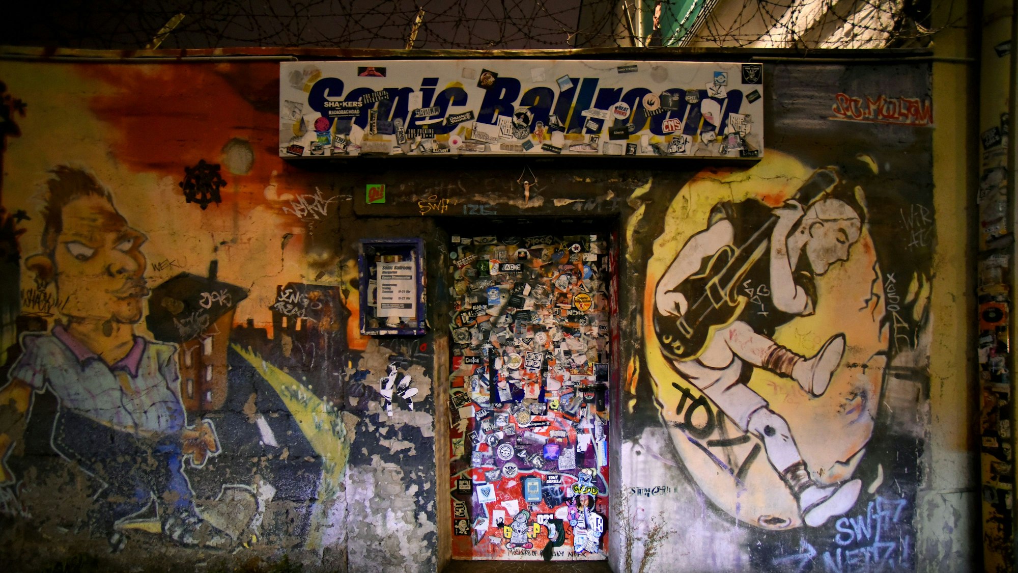 Außenaufnahme des Sonic Ballroom in der Nacht: Die Eingangstüre ist mit Stickern voll geklebt, auf der Fassade sind Graffitis angebracht.