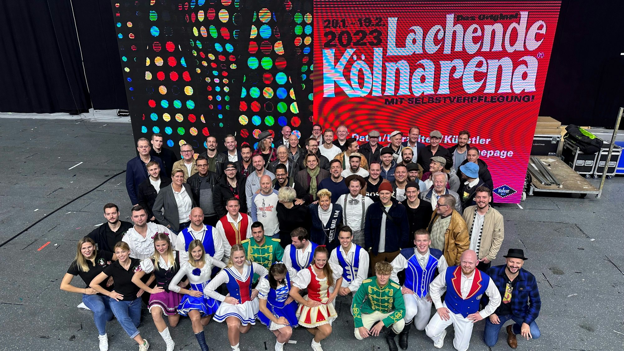 Plakat der Lachenden Kölnarena 2023, davor Künstler und Tanzgruppen.