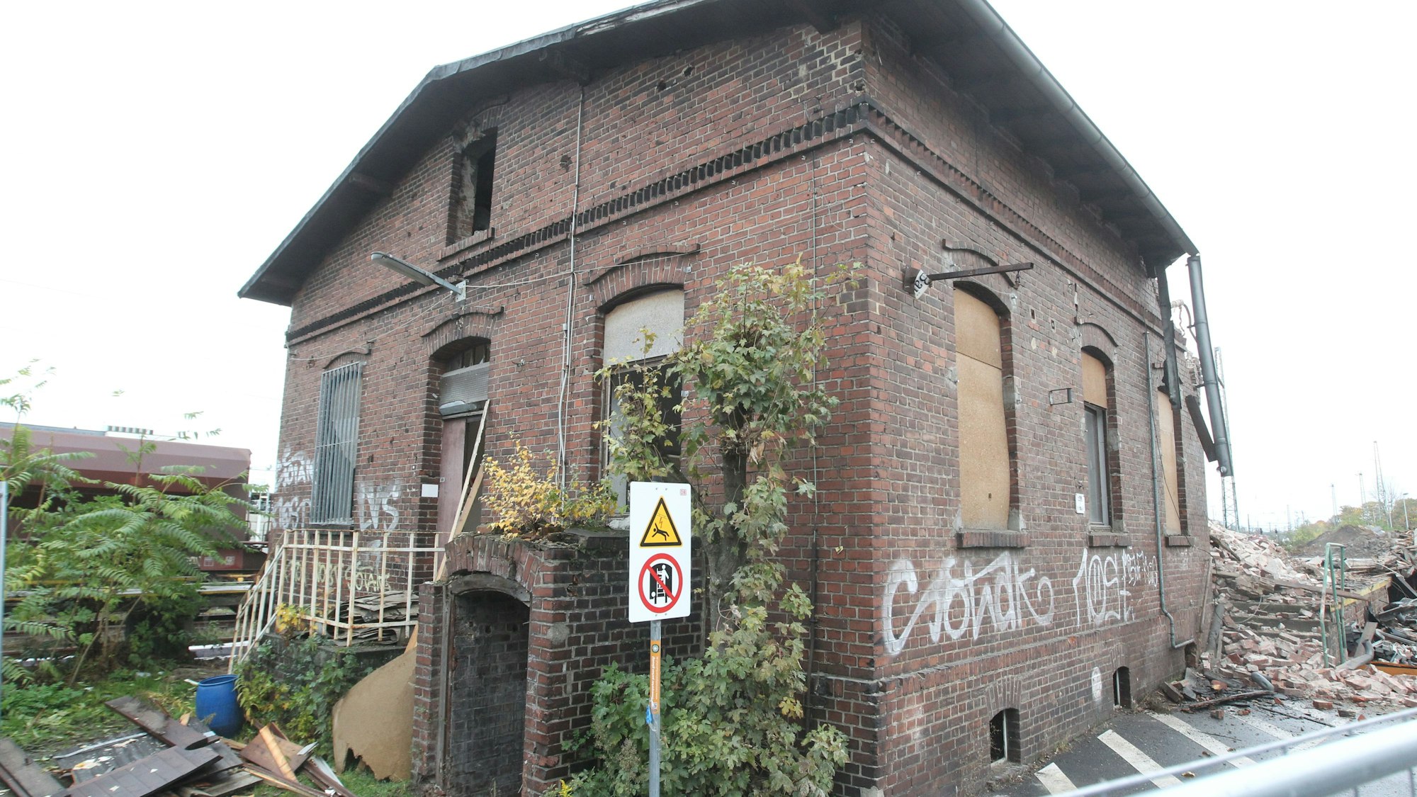 Ein altes Lagerhaus am Troisdorfer Güterbahnhof. Die Wände sind mit Graffiti besprüht. Ein Schild warnt vor der Gefahr durch die Oberleitungen.