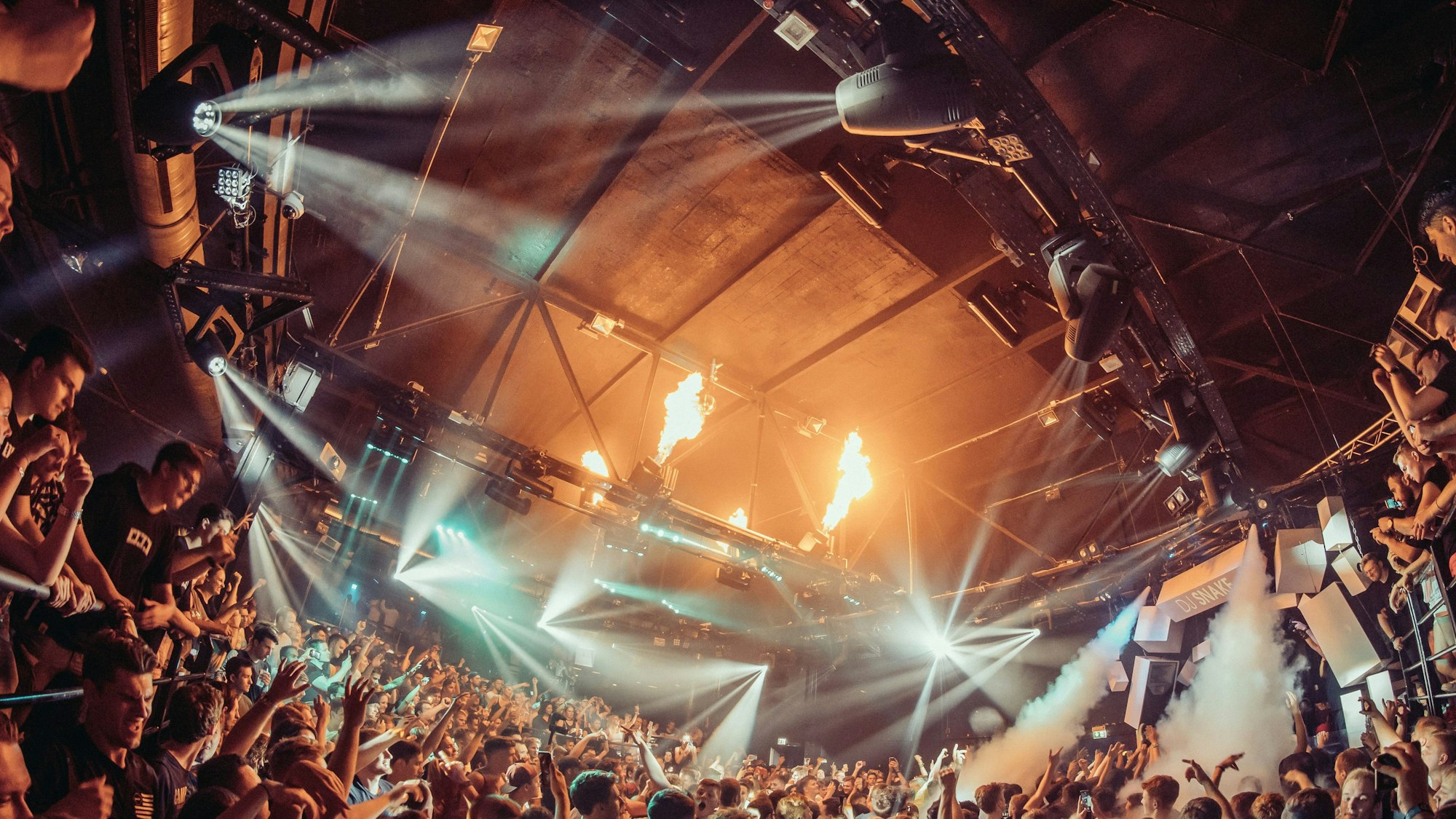 Eine tanzende Menschenmenge wird im Bootshaus von Scheinwerfern bestrahlt, eine Nebelmaschine ist im Einsatz.