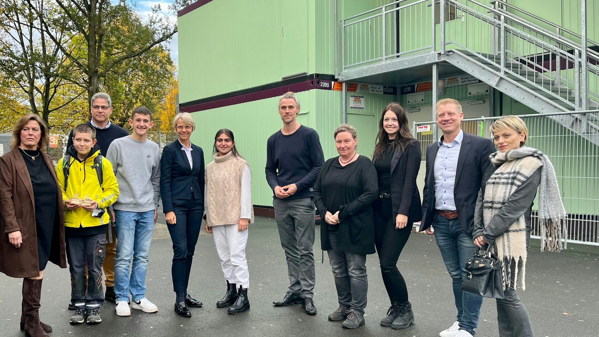 Mitglieder der Schulgemeinschaft stehen vor mintfarbenen Schulcontainern.