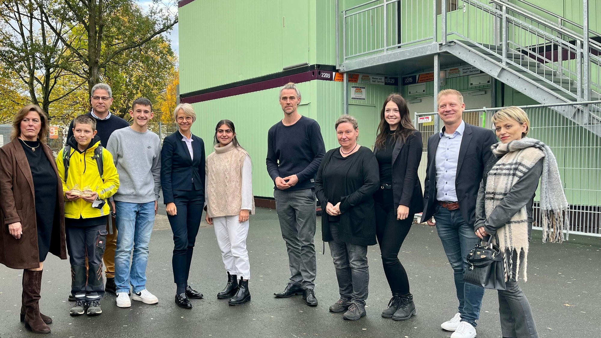 Eltern, Lehrer und Schüler mit Schulministerin Feller vor den mintgrünen Containern.
