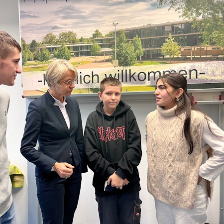Zwei Schüler und eine Schülerin diskutieren vor einem Plakat der Theodor-Heuss-Realschule mit der Schulministerin Dorothee Feller.