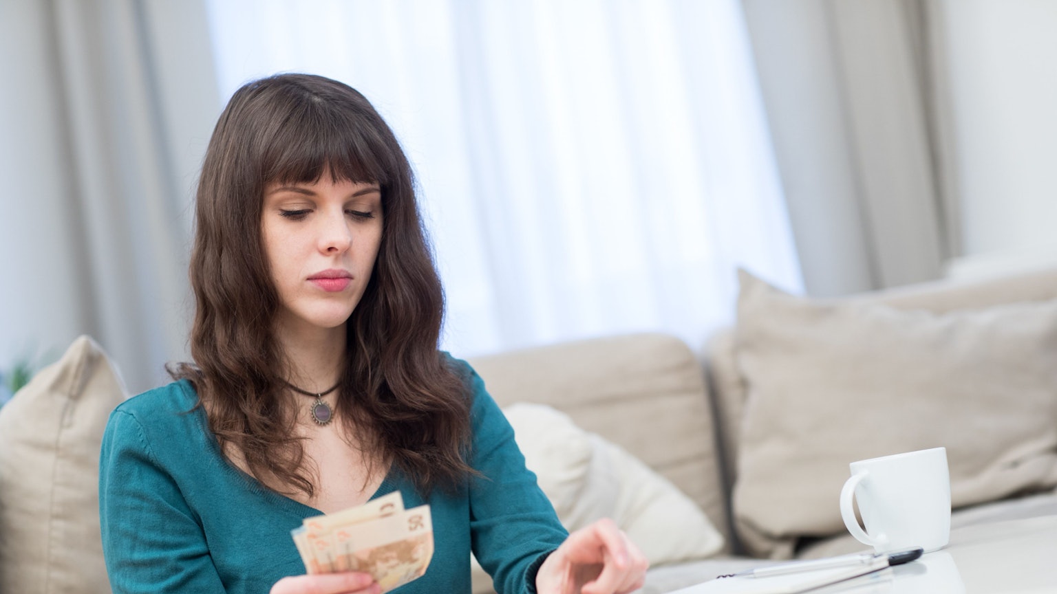 Eine junge Frau sitzt am Couchtisch und zählt Geldscheine.