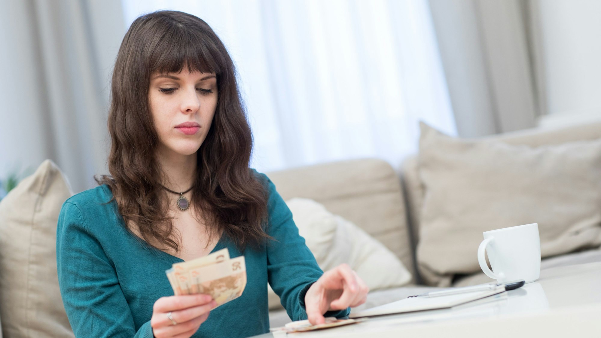 Eine junge Frau sitzt am Couchtisch und zählt Geldscheine.