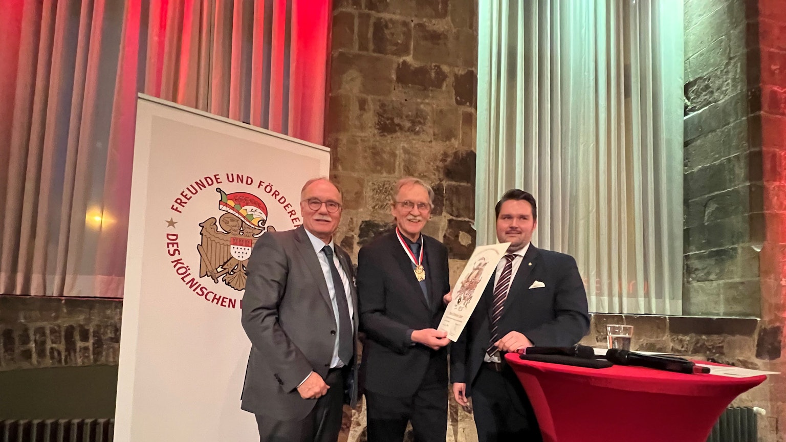 Im Gürzenich wird der Bürgerorden für Wolfgang Oelsner von Bernhard Conin überreicht, daneben steht Laudator Phillip Hoffman