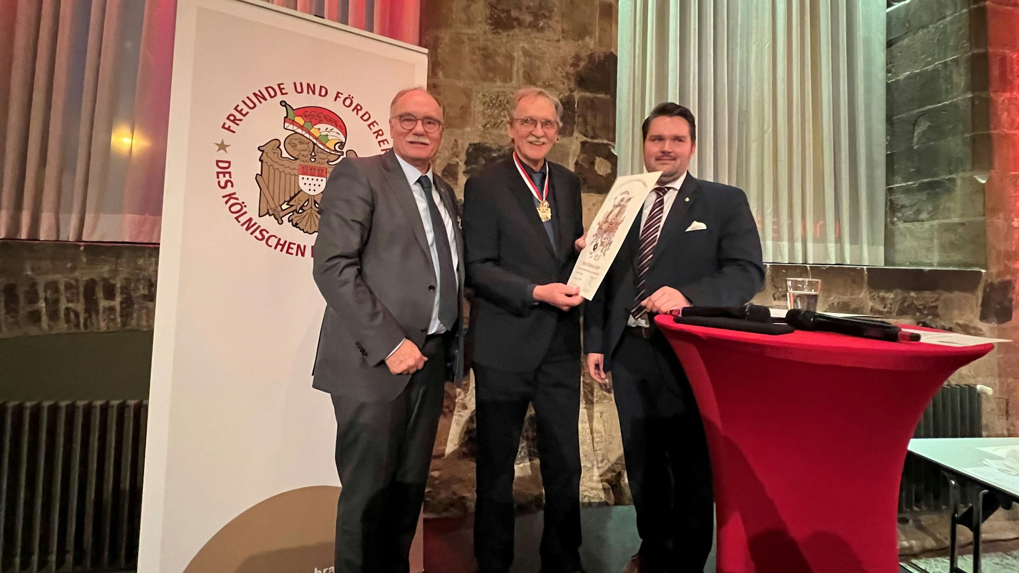 Im Gürzenich wird der Bürgerorden für Wolfgang Oelsner von Bernhard Conin überreicht, daneben steht Laudator Phillip Hoffman