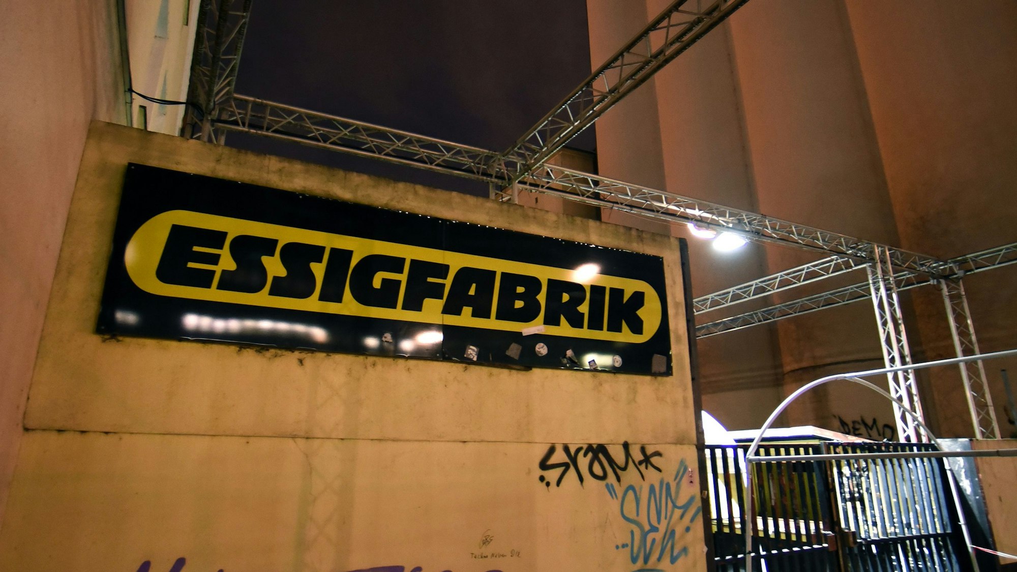 Die Fassade der Essigfabrik mit Schriftzug des Ladens in der Nacht, rechts befindet sich das Eingangstor.