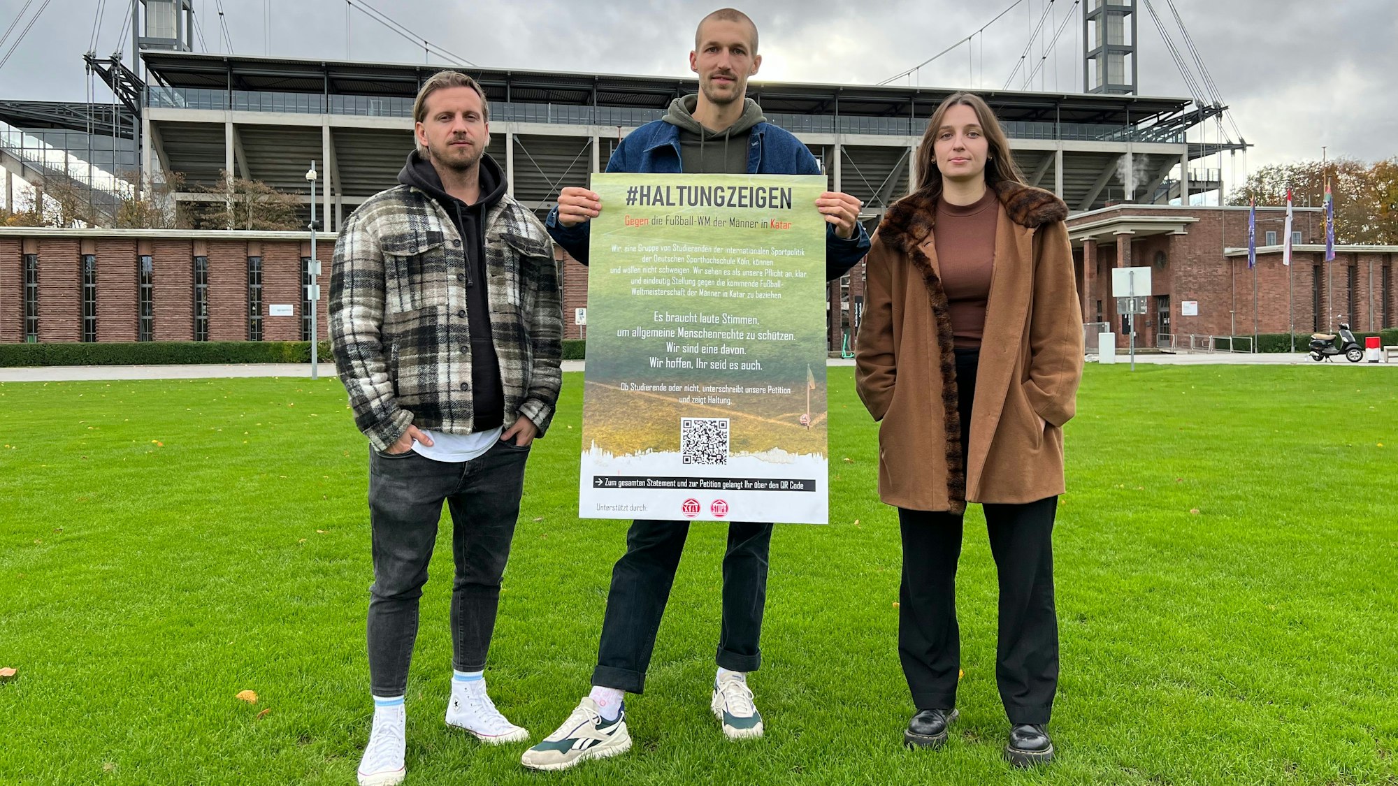 Vincent B., Luis K. und Clara P. stehen mit einem Plakat vor dem Kölner Stadion.