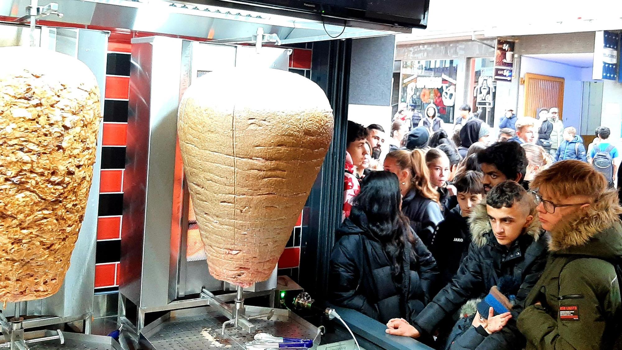 In Leverkusen-Opladen (Bahnhofstraße) eröffnete eine Filiale der Imbisskette „Haus des Döners“ – der Andrang am Eröffnungstag war riesig. Jugendliche stehen vor zwei riesigen Döner-Spießen Schlange.