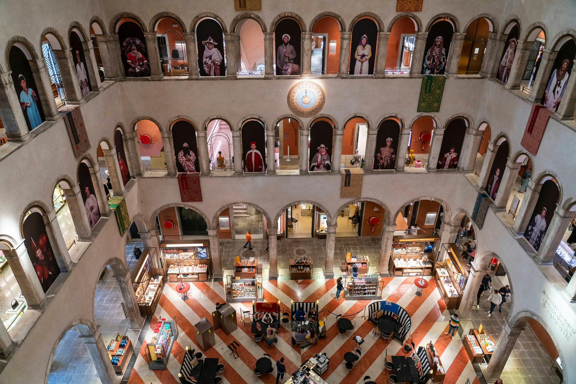 Blick aus dem vierten Stockwerk eines alten venezianischen Palastes in einen Innenhof, der mit Vitrinen und Gastronomie ausgestattet ist. Im Gebäude ist das Warenhaus Fondaco dei Tedeschi untergebracht. Arkaden begrenzen die Geschosse zum Innenhof.
