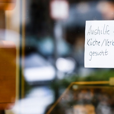 Ein Zettel mit der Aufschrift „Aushilfe für Küche/Verkauf gesucht“ hängt an der Scheibe einer Konditorei.