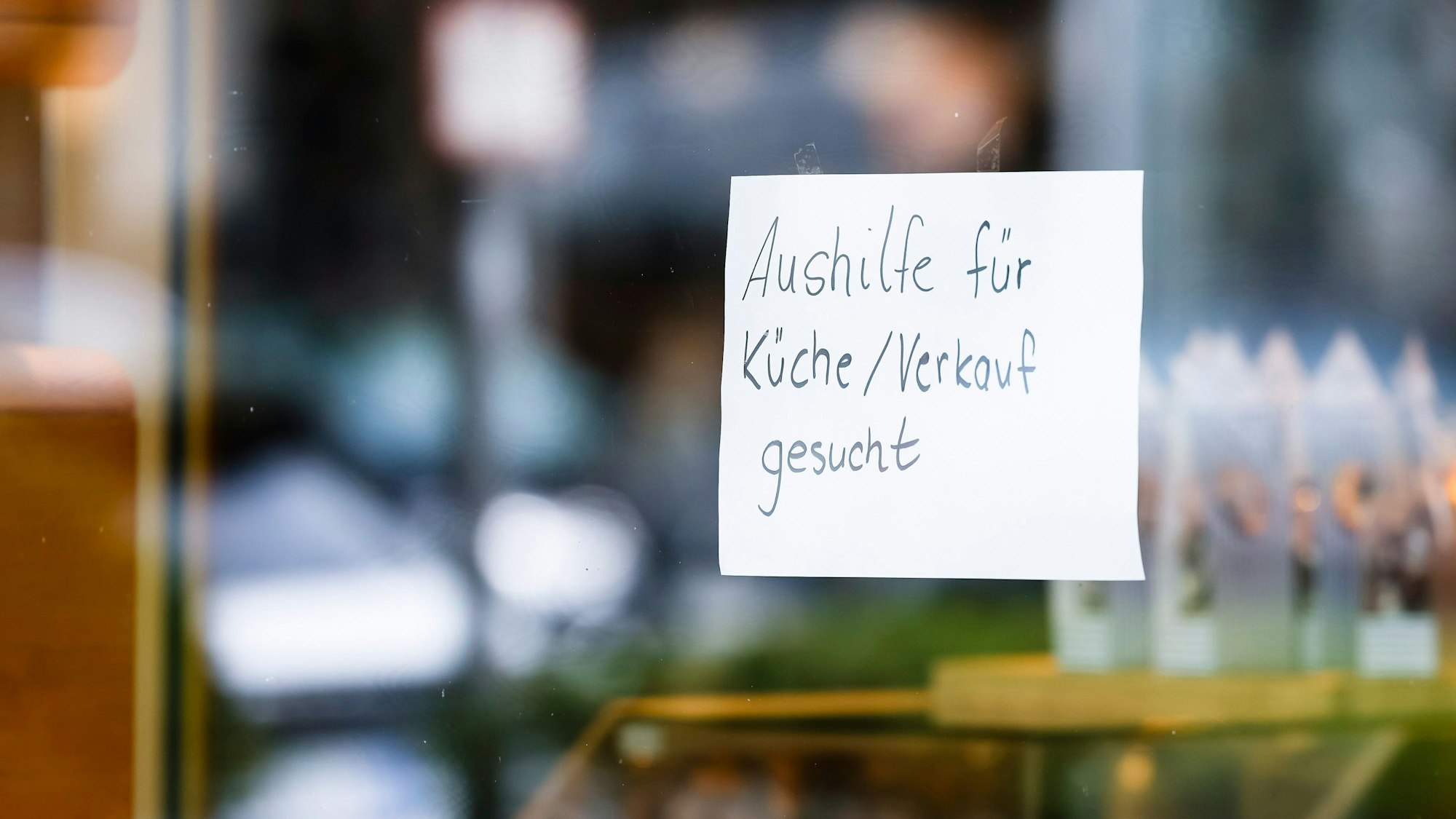 Ein Zettel mit der Aufschrift „Aushilfe für Küche/Verkauf gesucht“ hängt an einer Scheibe.