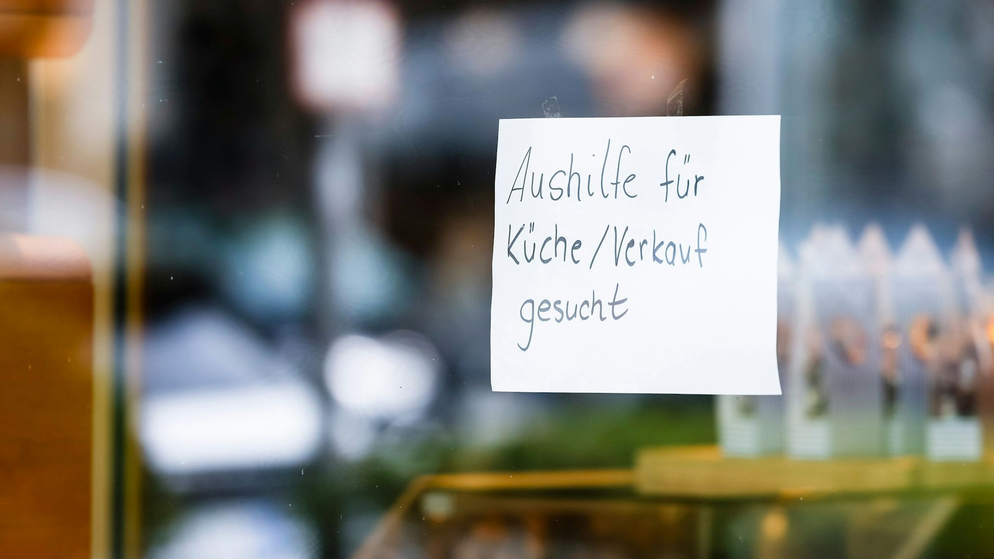 Ein Zettel mit der Aufschrift „Aushilfe für Küche/Verkauf gesucht“ hängt an der Scheibe einer Konditorei.