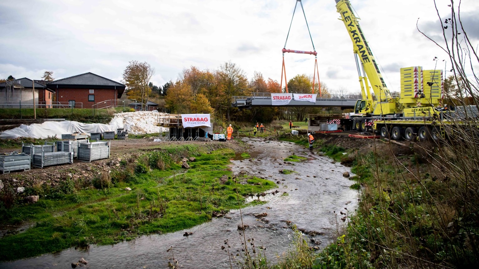 Ein gelber Kran hebt eine Brücke über die Erft.