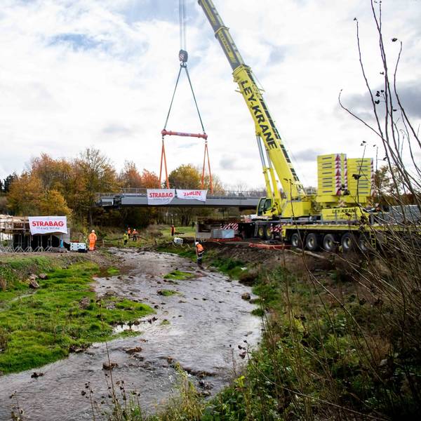 Ein gelber Kran hebt eine Brücke über die Erft.