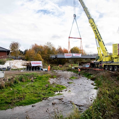 Ein gelber Kran hebt eine Brücke über die Erft.