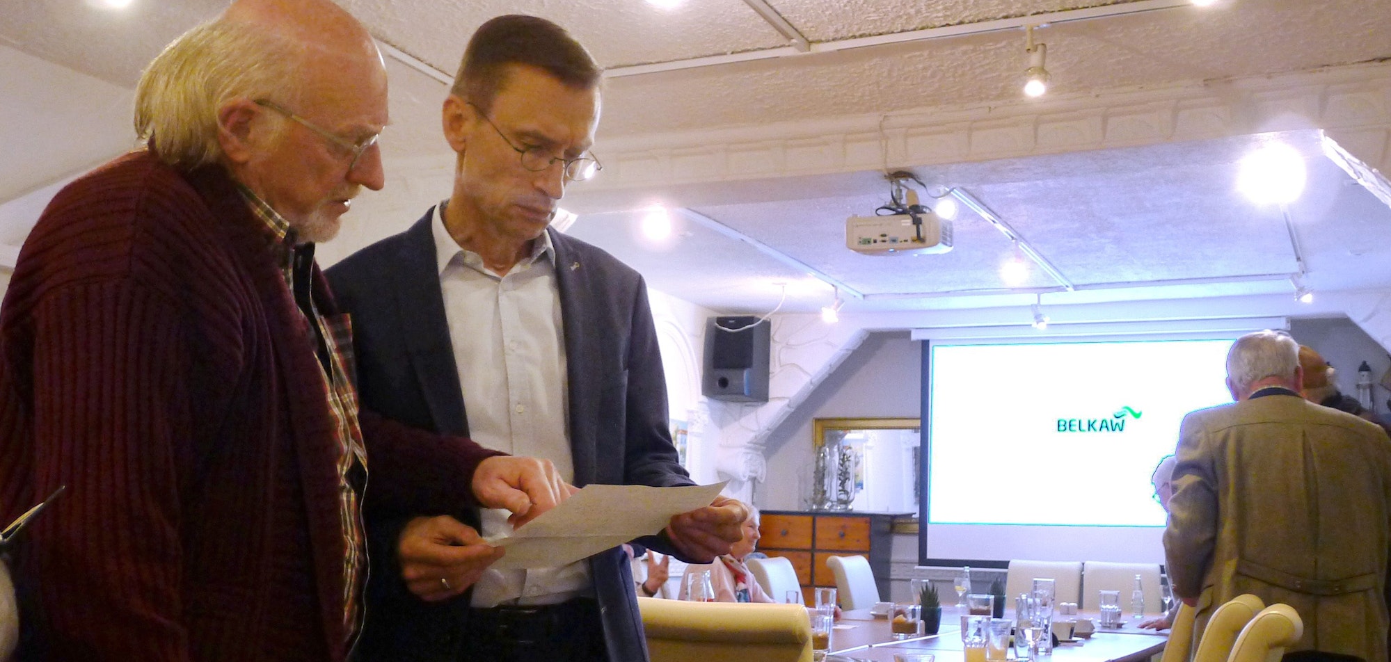 Zwei Männer in einem Saal schauen konzentriert auf ein Papier.