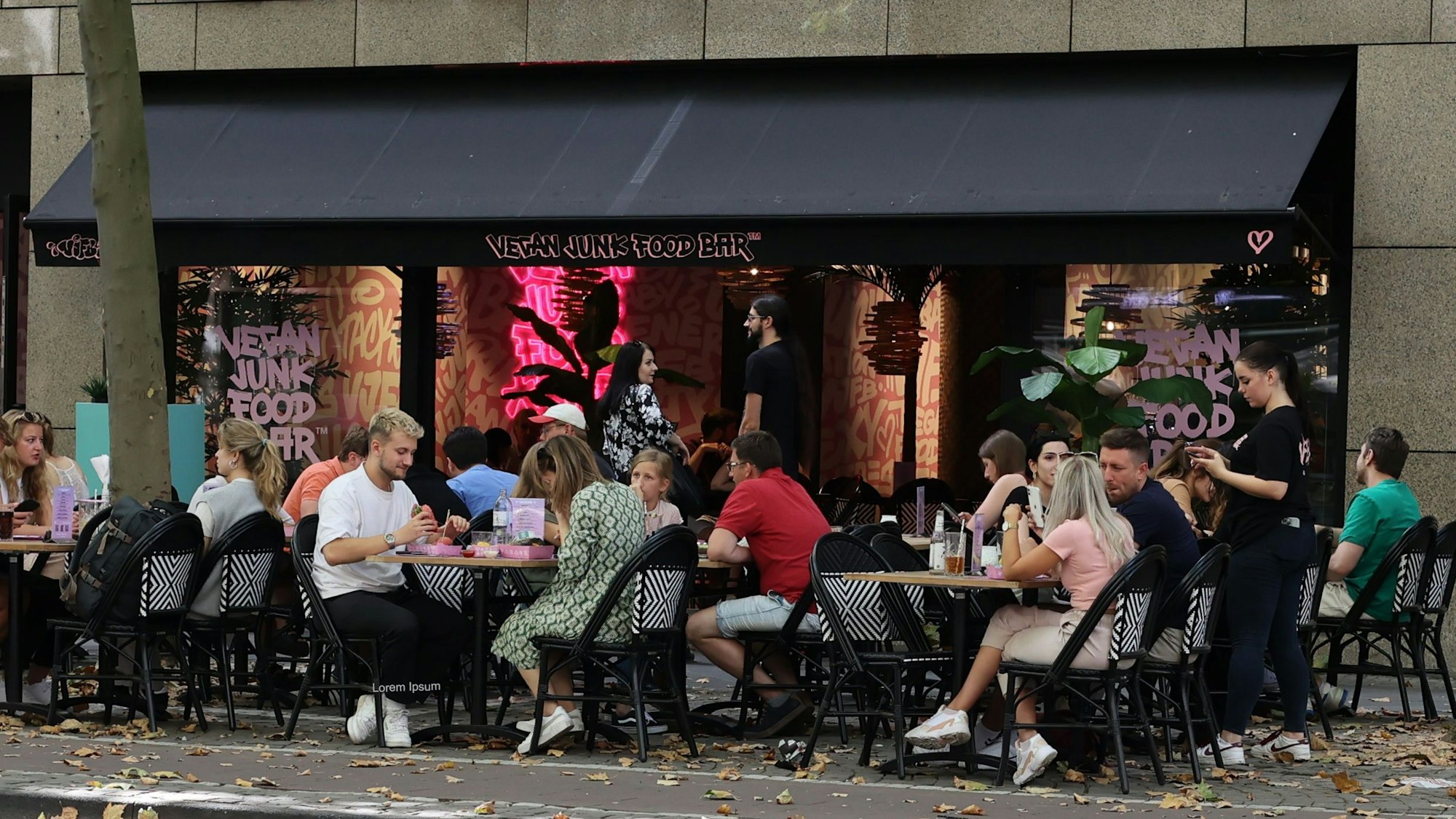 Menschen sitzen an Tischen vor der „Vegan Junk Food Bar“-Filiale in Köln