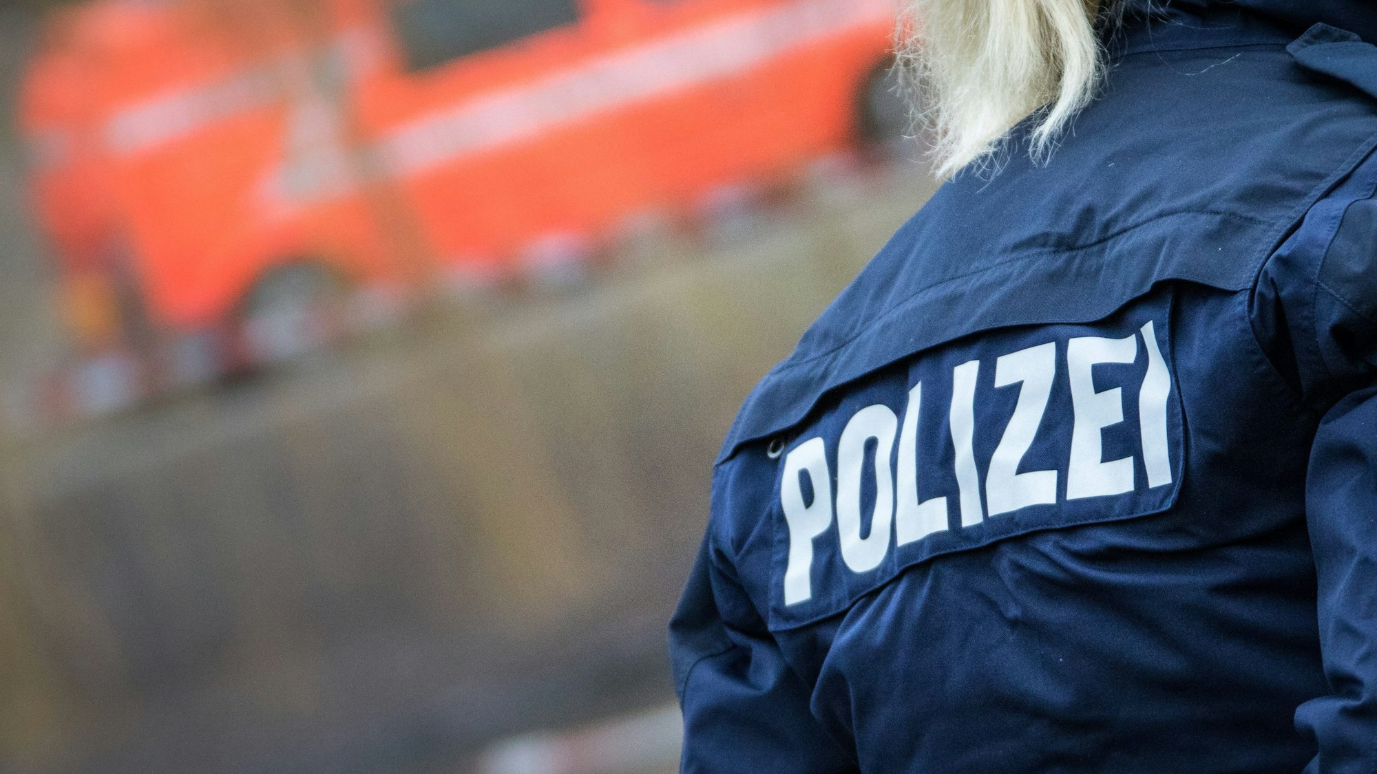 Das Bild zeigt den Rücken einer blonden Polizistin,