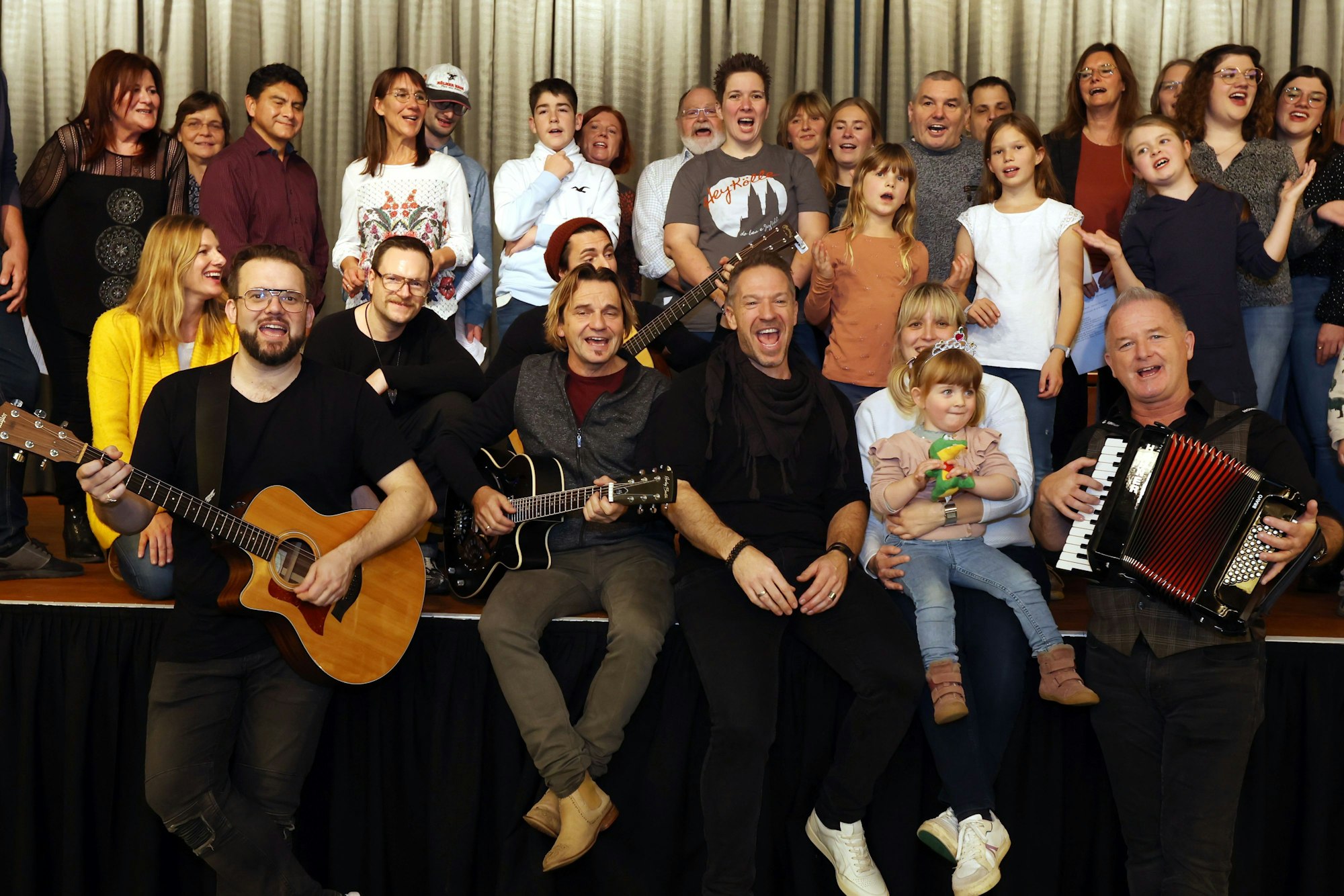 Der Familien-Workshop im Kölner Maritim-Hotel gehört zu den Höhepunkten der Jubiläumsausstellung „50 Jahre Höhner“ des Kölnischen Stadtmuseums. Menschen singen in drei Reihen sitzend und stehend auf einer Bühne.