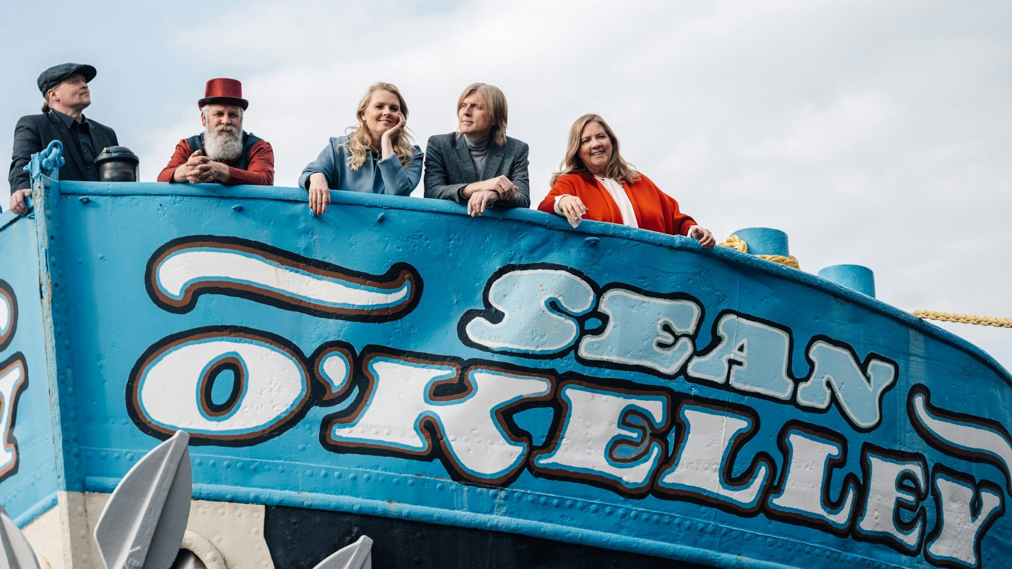 Man sieht Joey, Paul, Patricia, John und Kathy Kelly auf einem Boot. Das Boot ist blau angestrichen und hat den Schriftzug „Sean O´Kelly“. Im Hintergund sieht man den Himmel.