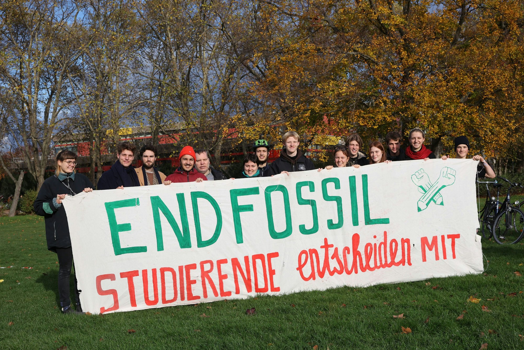 Fridays for Future und End Fossil beim Klimastreik auf der Kölner Uniwiese. Viele junge Menschen halten ein Plakat mit der Aufschrift: „END FOSSIL STUDIERENDE entscheiden mit“