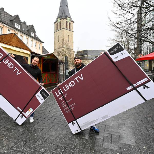 Der Gastronom Timo Bay hält einen großen verpackten Bildschirm in der Hand, ebenso sein Freund. Sie stehen in der Gummersbacher Innenstadt vor einem Glühweinstand und zeigen hier ab Sonntag die Fußball-WM.