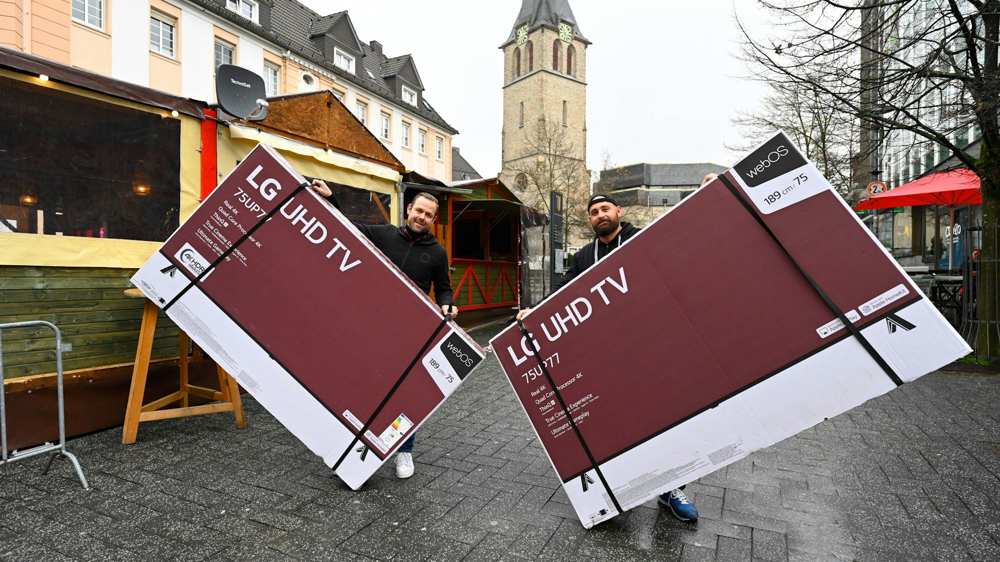 Der Gastronom Timo Bay hält einen großen verpackten Bildschirm in der Hand, ebenso sein Freund. Sie stehen in der Gummersbacher Innenstadt vor einem Glühweinstand und zeigen hier ab Sonntag die Fußball-WM.