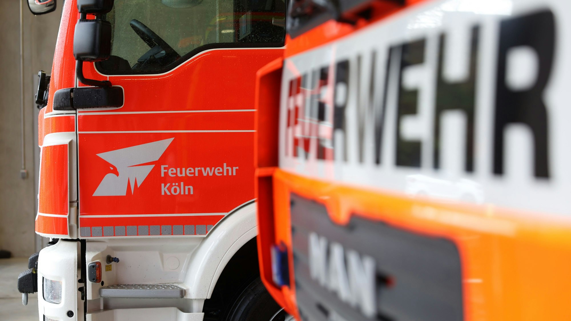 Feuerwehrautos mit dem Emblem der Kölner Feuerwehr stehen in einer Halle.
