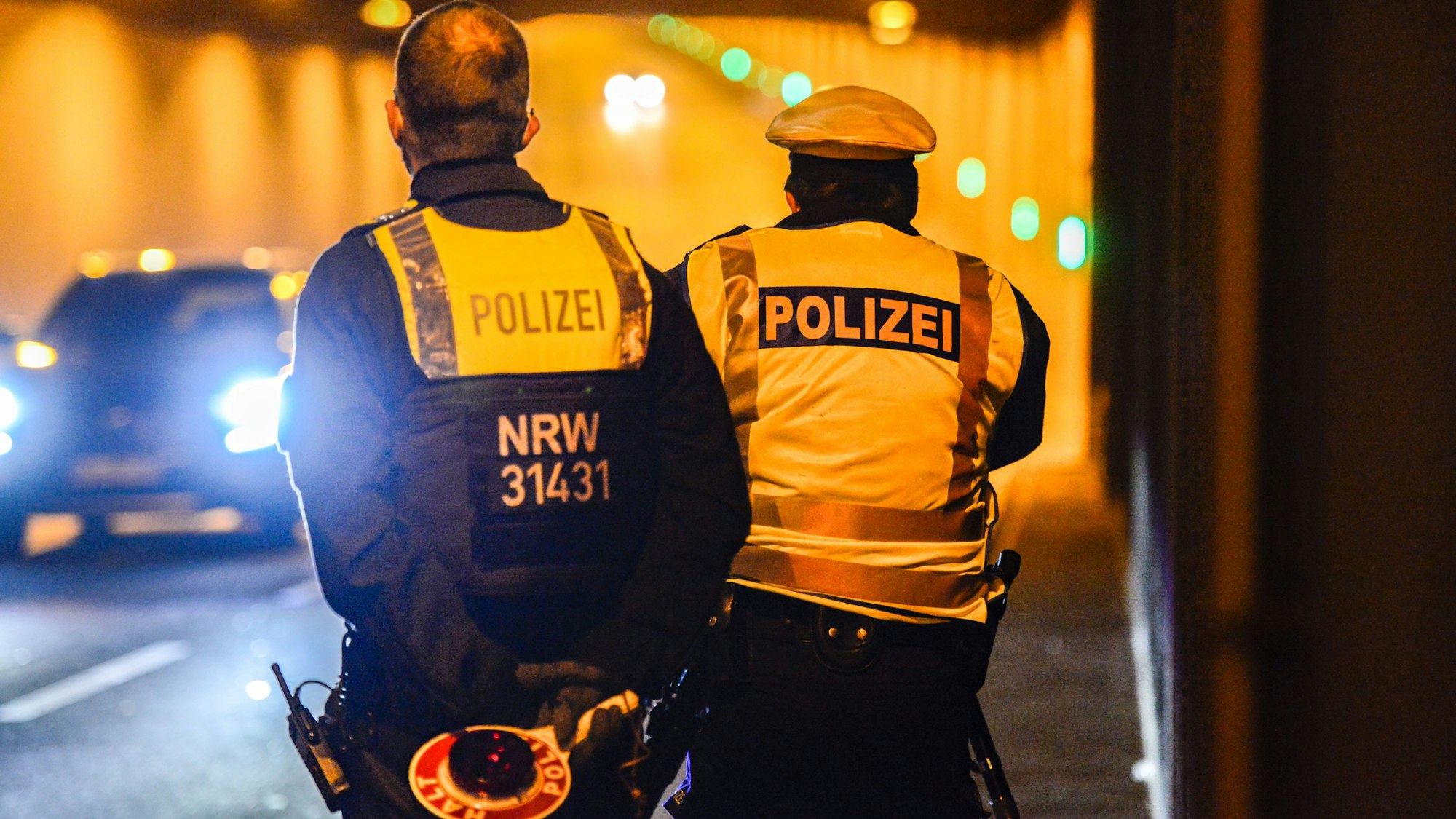 Zwei Polizisten stehen mit einer Kelle in einem Tunnel. Ein Auto kommt ihnen entgegen.