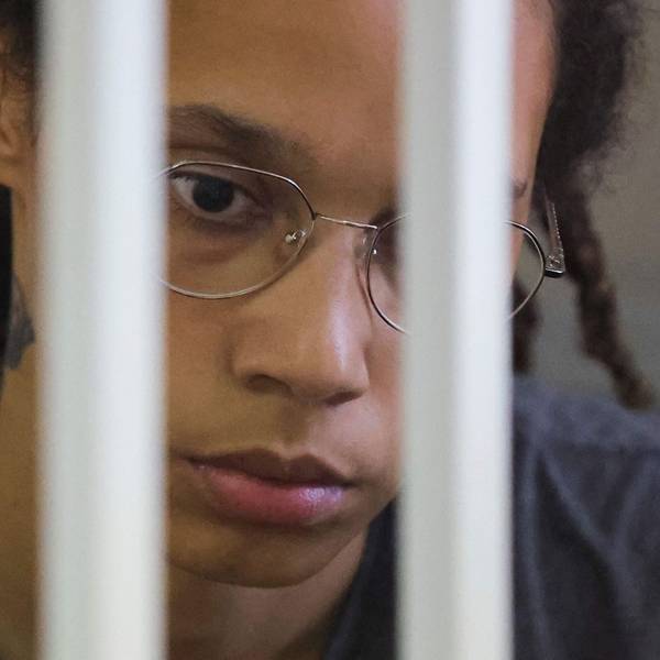 Brittney Griner Gesicht ist zu sehen, sie guckt traurig nach unten und wirkt abwesend. Vor ihrem Gesicht sieht man unscharf Gitterstäbe.