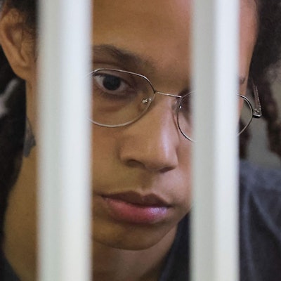 Brittney Griner Gesicht ist zu sehen, sie guckt traurig nach unten und wirkt abwesend. Vor ihrem Gesicht sieht man unscharf Gitterstäbe.