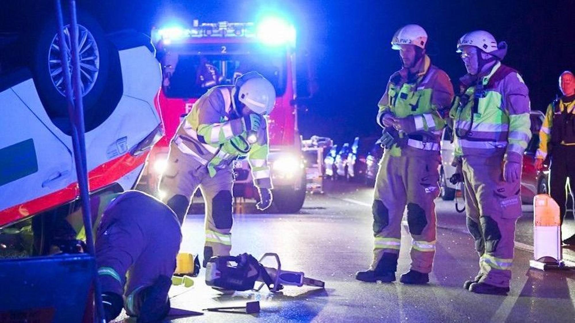 Einsatzkräfte der Feuerwehr stehen neben dem Auto, das auf dem Dach liegt.