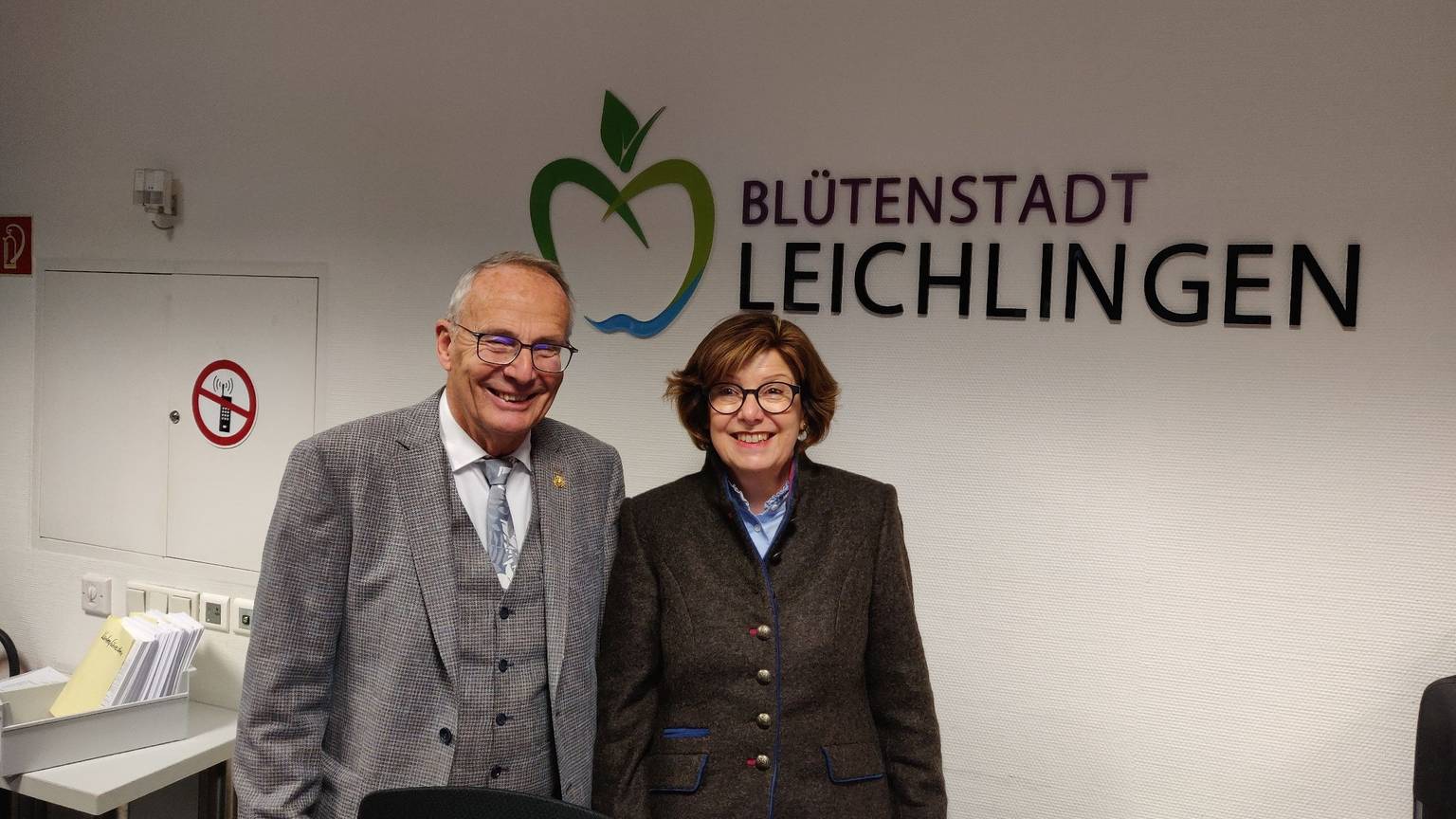 Schiedsfrau Gisela Becher steht mit ihrem Vorgänger Gert Schulze im Rathausfoyer vor dem Schriftzug Blütenstadt Leichlingen