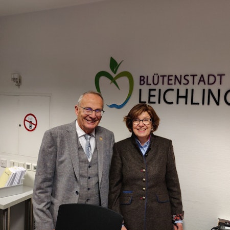 Schiedsfrau Gisela Becher steht mit ihrem Vorgänger Gert Schulze im Rathausfoyer vor dem Schriftzug Blütenstadt Leichlingen
