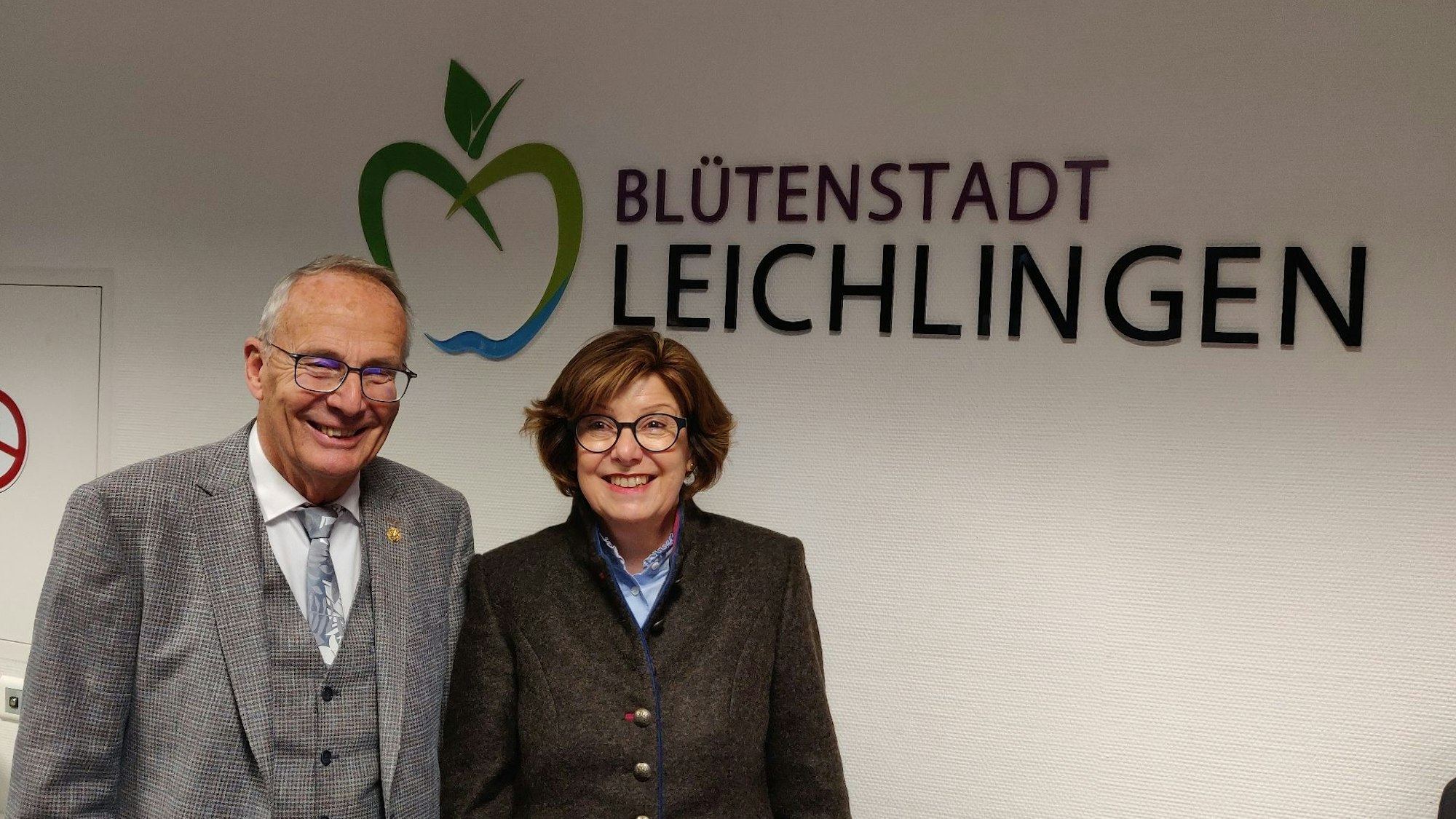 Schiedsfrau Gisela Becher steht mit ihrem Vorgänger Gert Schulze im Rathausfoyer vor dem Schriftzug Blütenstadt Leichlingen