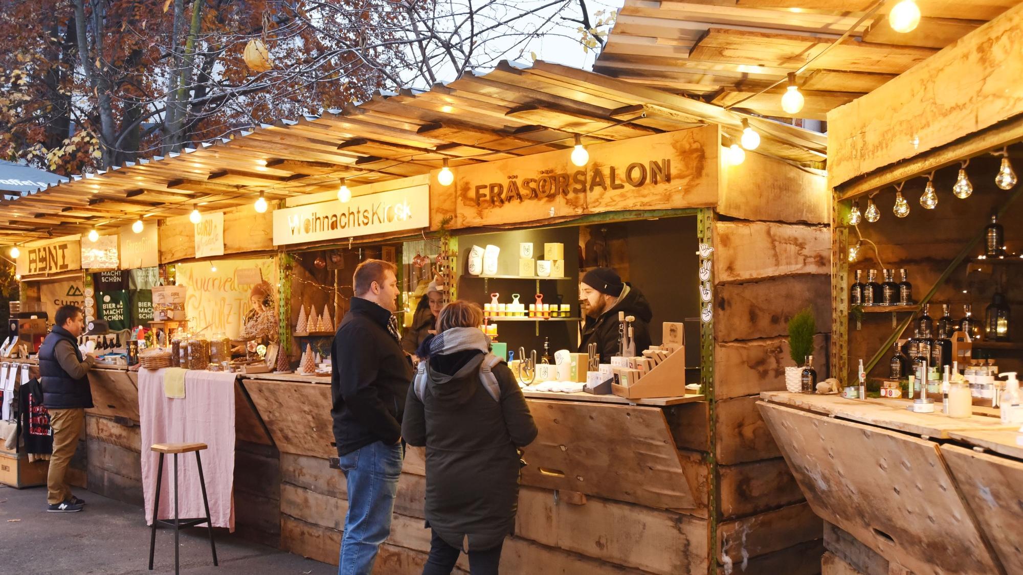 Menschen stehen vor hölzernen Weihnachtsmarktständen mit Kerzen und Lichtern.