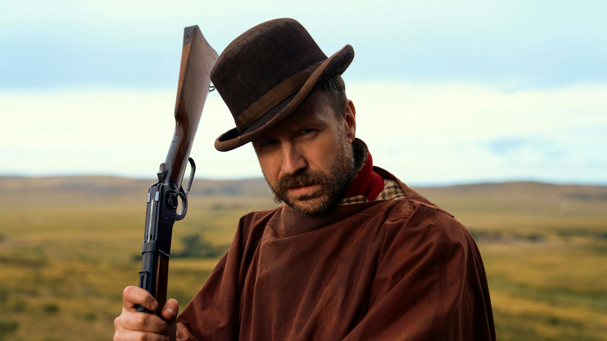 Rafe Spall mit einem Gewehr in der Hand.