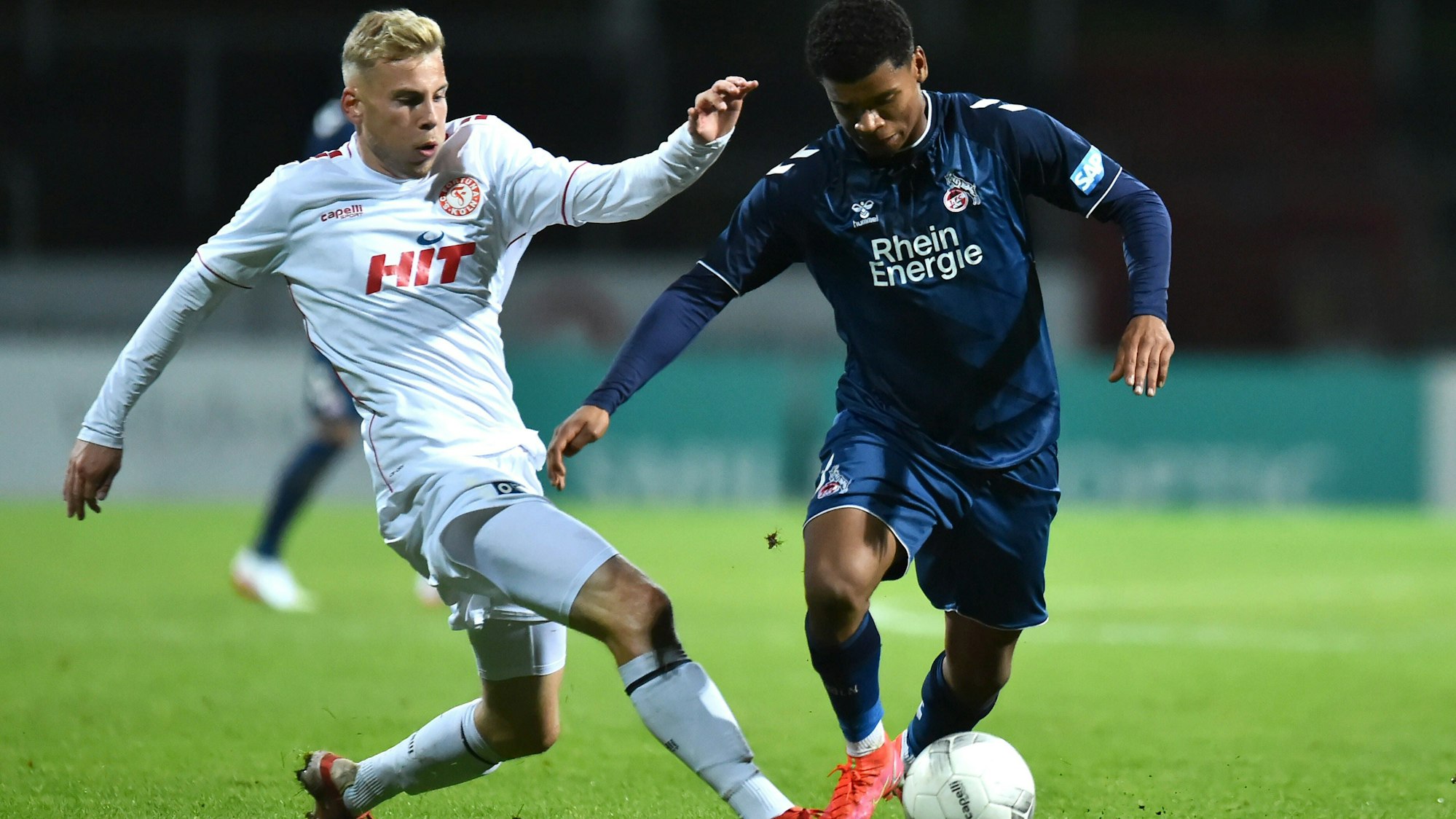 Fußballspieler befinden sich im Zweikampf. Der linke versucht, dem rechten den Ball abzunehmen.