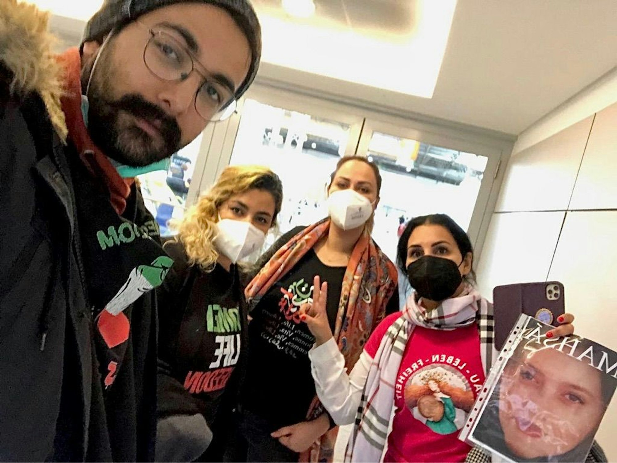 Ein Mann und drei Frauen demonstrieren mit Revolutions-T-.Shirts und einem Bild der mutmaßlich vom iranischen Sicherheitsdienst getöteten Mahsa Amini auf der Düsseldorfer Medizinmesse gegen einen Iran-Pavillon.