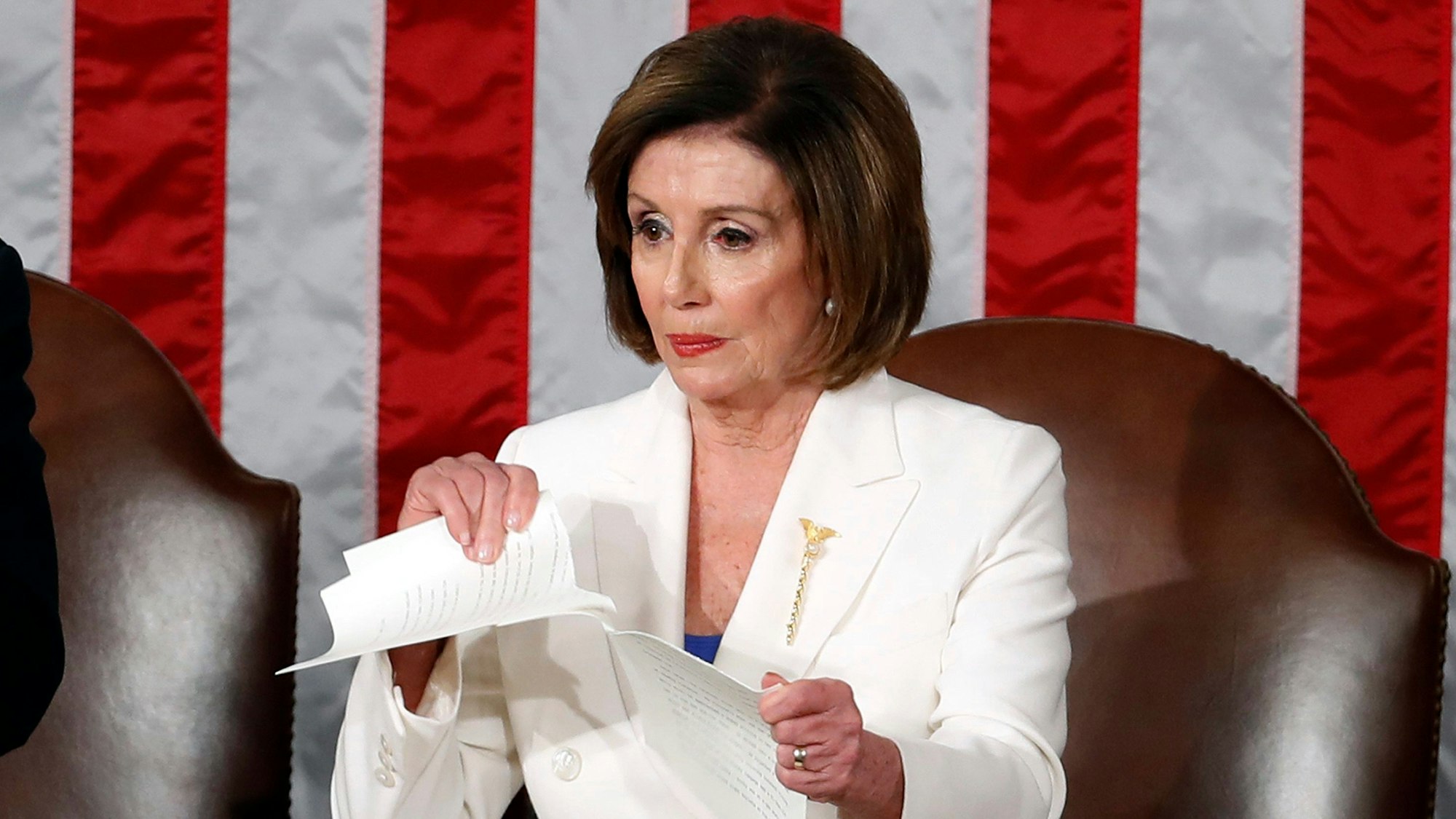 Nancy Pelosi, demokratische Vorsitzende des Repräsentantenhauses, zerreißt das Redemanuskript von Donald Trump. Sie trägt einen weißen Blazer und blickt ernst.