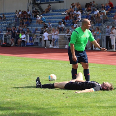 Euskirchens Kapitän Fritz Hilgers liegt auf dem Rasen des Erftstadions und hält sich schmerzverzerrt die Leiste. Der Schiedsrichter steht neben ihm und spricht mit den herannahenden Betreuern.