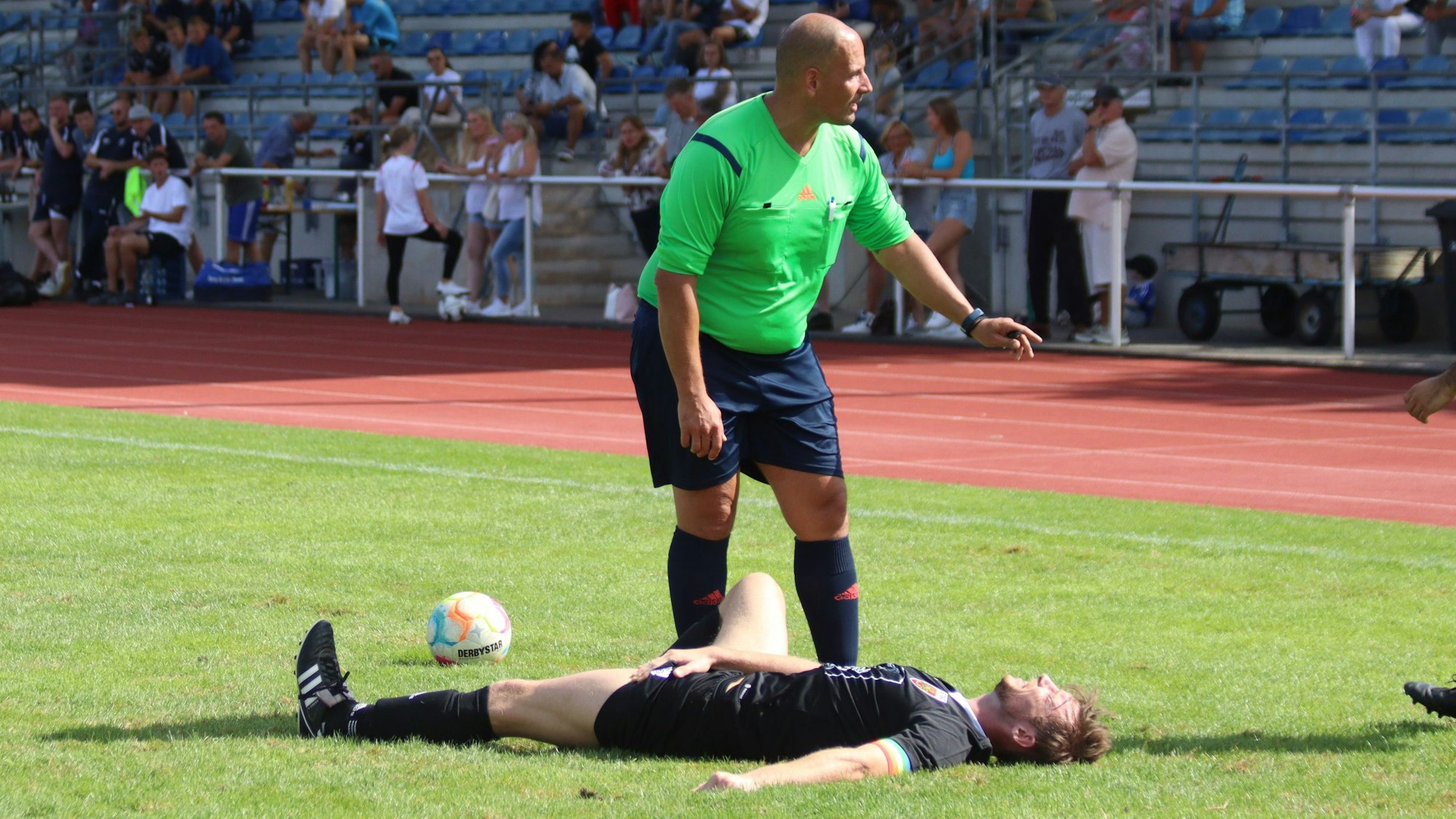 Euskirchens Kapitän Fritz Hilgers liegt auf dem Rasen des Erftstadions und hält sich schmerzverzerrt die Leiste. Der Schiedsrichter steht neben ihm und spricht mit den herannahenden Betreuern.