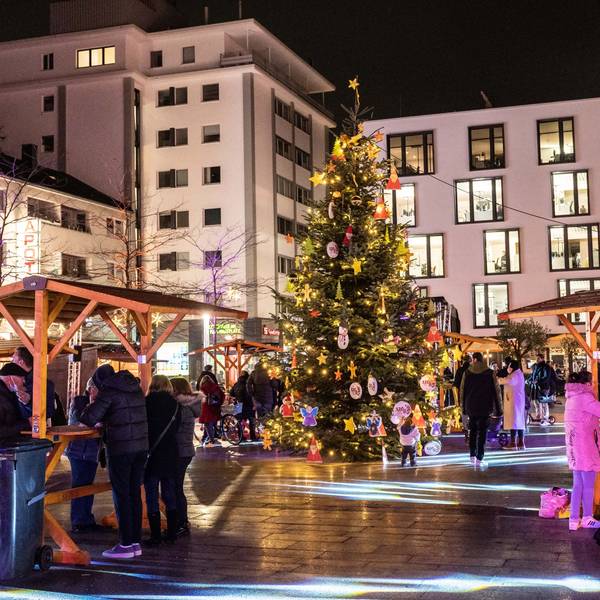 In der Mitte des Maternusplatzes steht ein Weihnachtsbaum. Besucher trinken Glühwein.