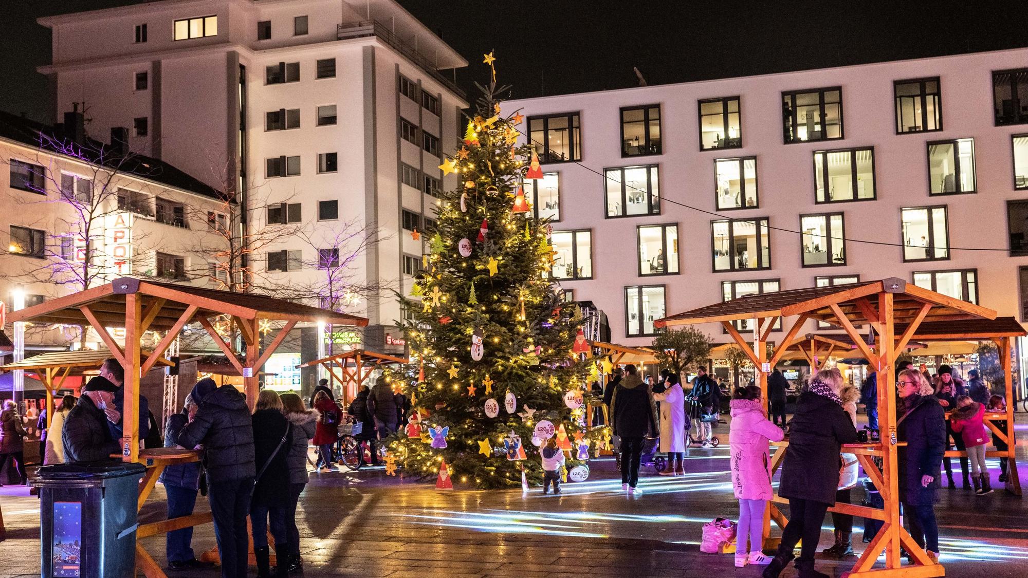 Ein kleiner Weihnachtsmarkt mit überdachten Tischen und einem großen, leuchtenden Weihnachtsbaum in Rodenkirchen.